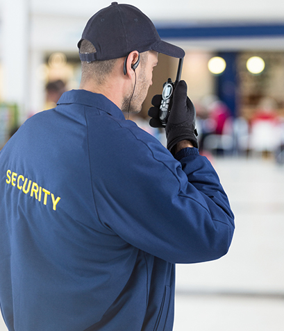Digital Composite of Back of Security Guard With Walkie Talkie Against Blurry Shopping Center